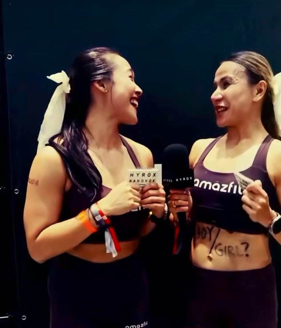 Dina and her doubles partner laughing at the Hyrox Bangkok finish line, BOY / GIRL? written on her stomach