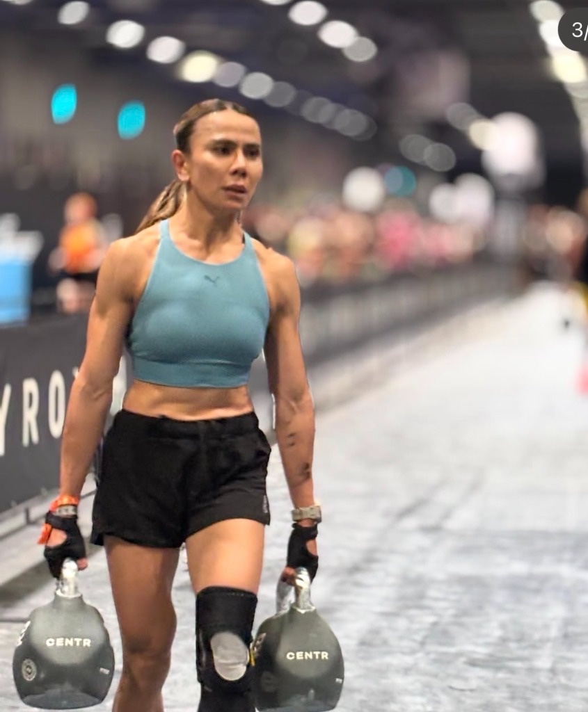 Dina mid-stride on the farmers carry with competition kettlebells