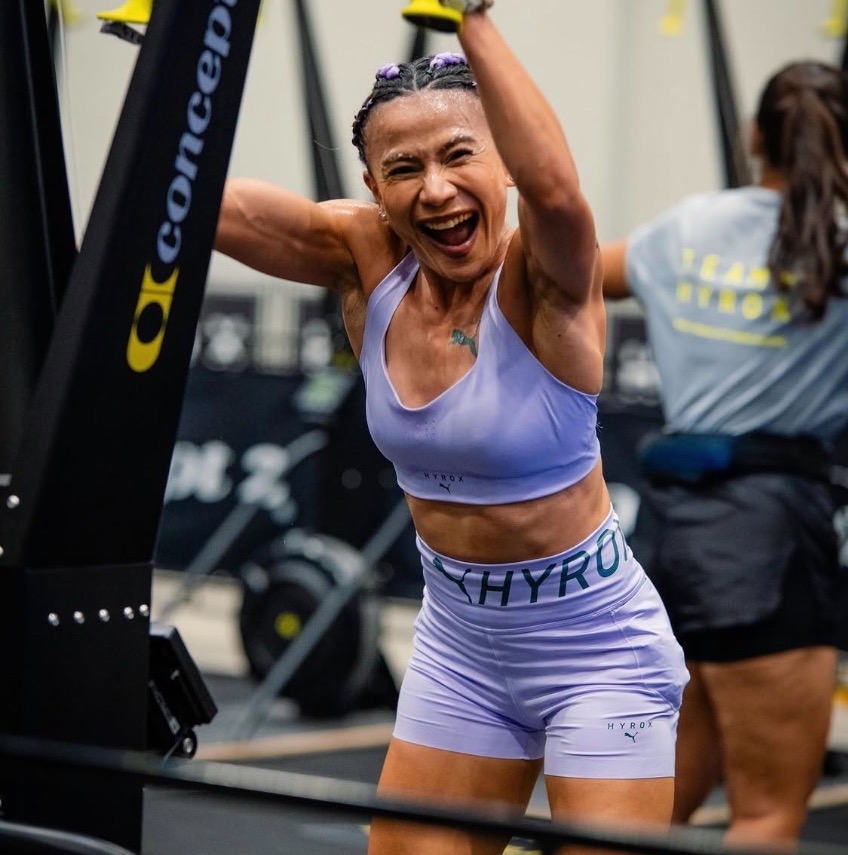 Dina with arms up at the SkiErg mid-workout