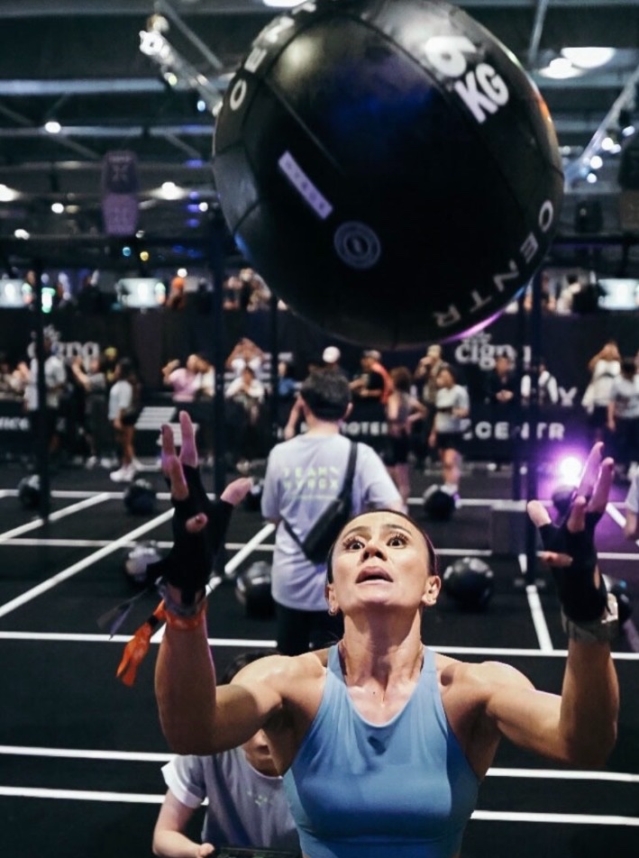 Dina launching a 6 kg wall ball overhead in the dark arena